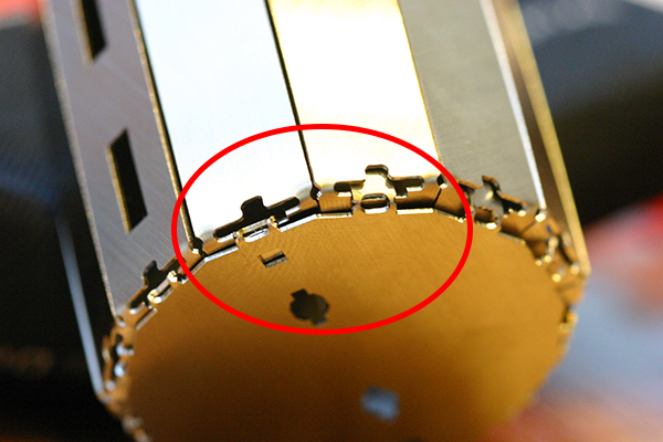 専用の冶具と手だけで組立てられるよう、随所に工夫が凝らされている。写真はロボットの胴体の底部分。底パーツをはめただけ（赤枠内右側）だとすぐ取れてしまうので、冶具の先端で底パーツのツメを内側に押し込み、引っ掛けて固定する（左側）